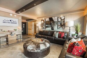 Un salon moderne avec un canapé, un pouf et des œuvres d’art accrochées au mur.