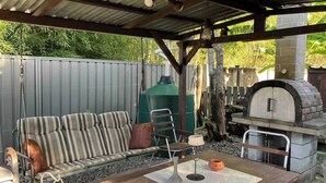 Un patio al aire libre con mesa de madera, sofá a rayas y un horno de ladrillo.