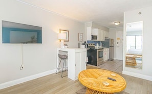 A compact living space with a kitchenette, a dining area with a round table, a TV mounted on the wall, and a small seating area.