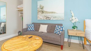 A living room with a grey sofa, a round wooden coffee table, a painting of a beach scene, and a small wooden side table with a vase of white flowers. - Sea Mist 51108 (Myrtle Beach)