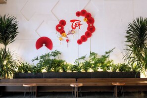 A reception area with a wooden bench, a small round table, and a wall decorated with red paper fans and plants. - Mien Tay Hotel (Can Tho)