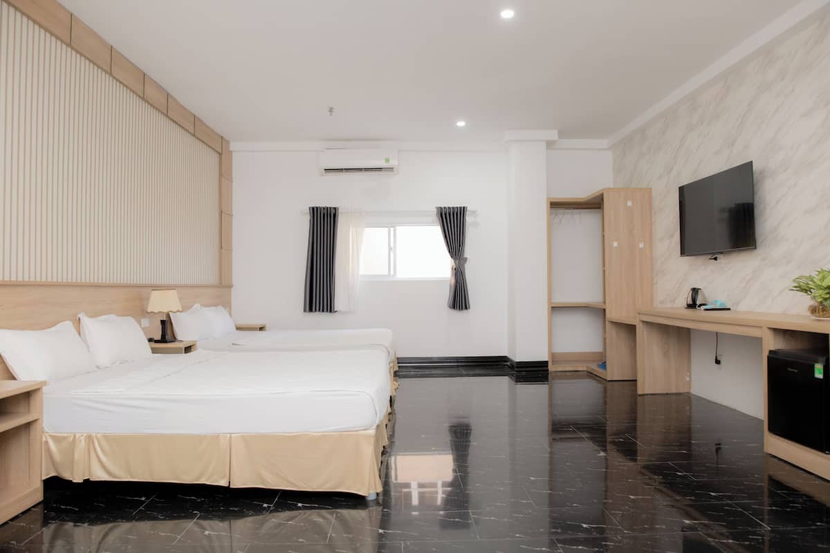 A modern hotel room with a large bed, a desk, a flat-screen TV, and a small refrigerator.