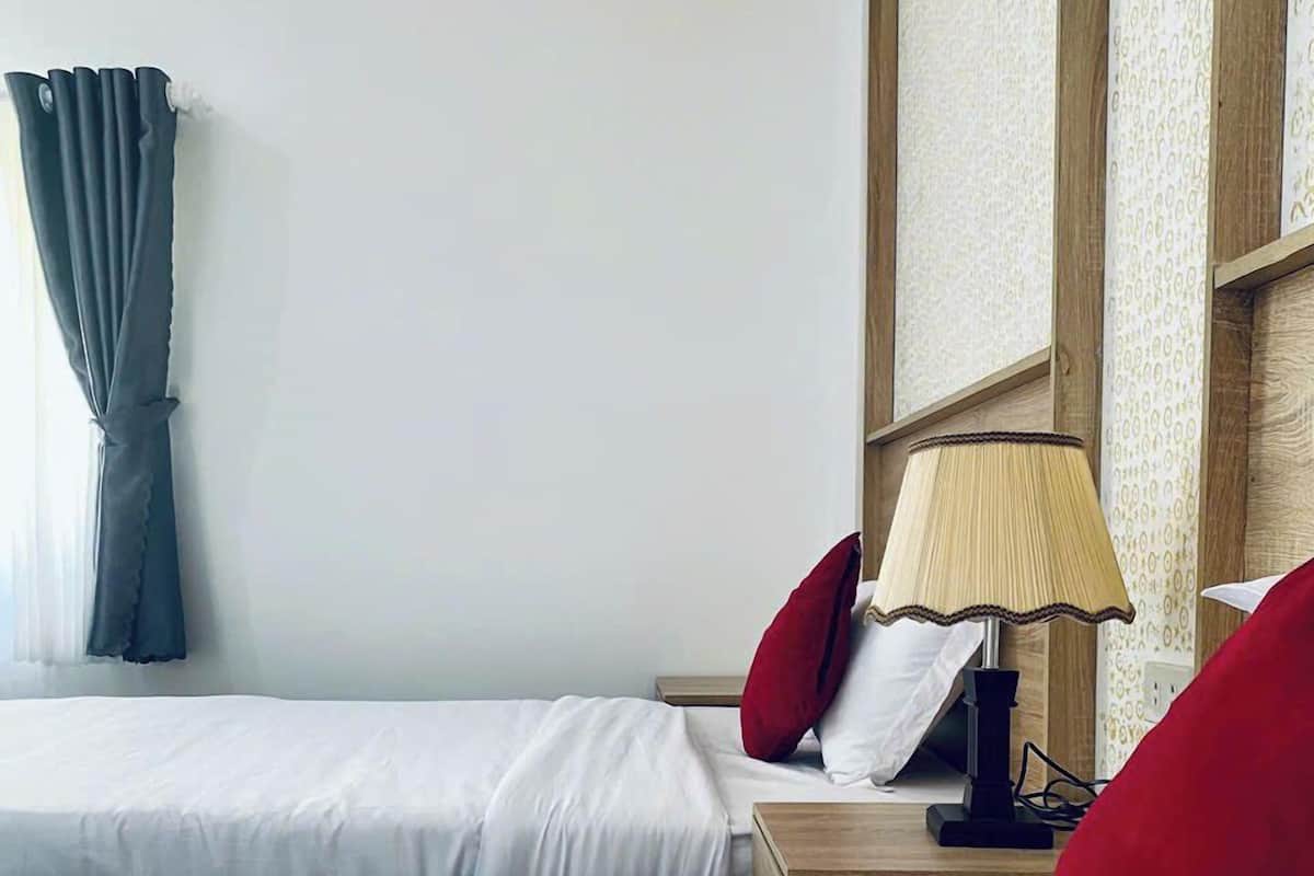 A hotel room with two beds, a nightstand with a lamp, and a window with curtains.