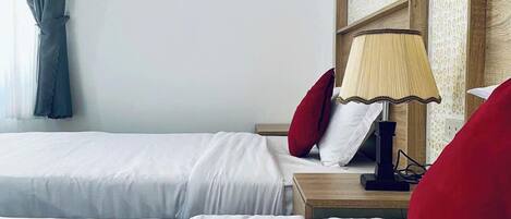Una habitación de hotel con dos camas, una mesita de noche con lámpara y una ventana con cortinas.