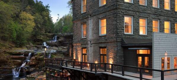 A stone building with multiple windows, a waterfall, and a wooden deck.