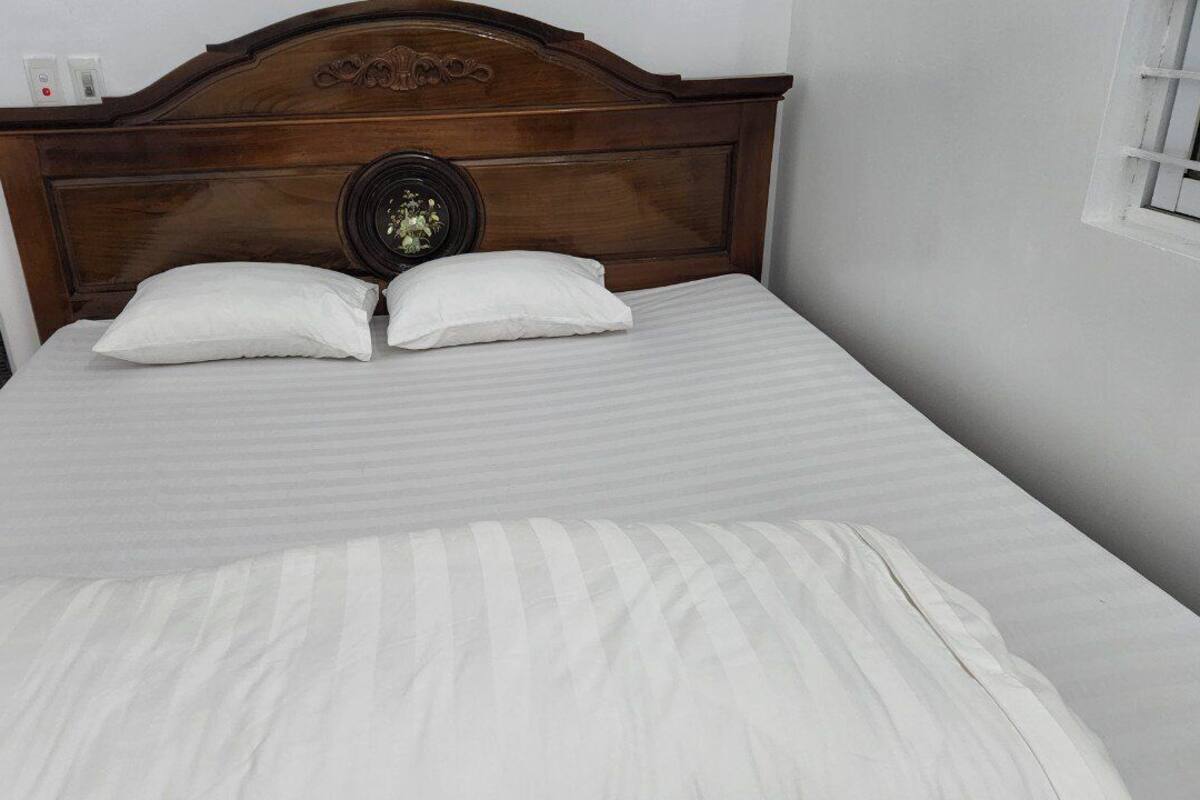 Un lit bien fait, avec une tête de lit en bois, deux oreillers et un couvre-lit blanc.