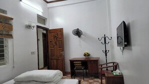 Une pièce comprenant un lit, un bureau, une chaise, un téléviseur, un ventilateur et une porte.