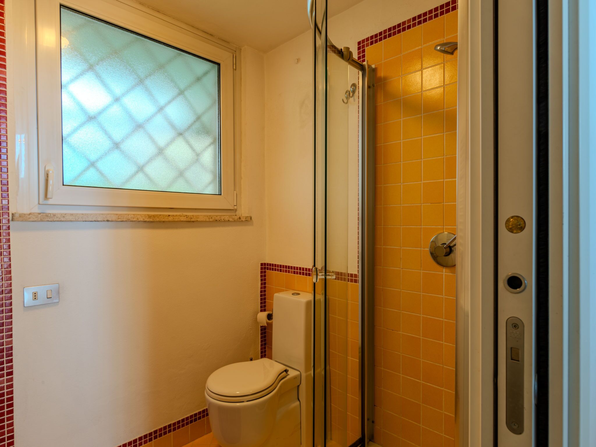 Et badeværelse med toilet, brusekabine i glas og et vindue med satin glas.