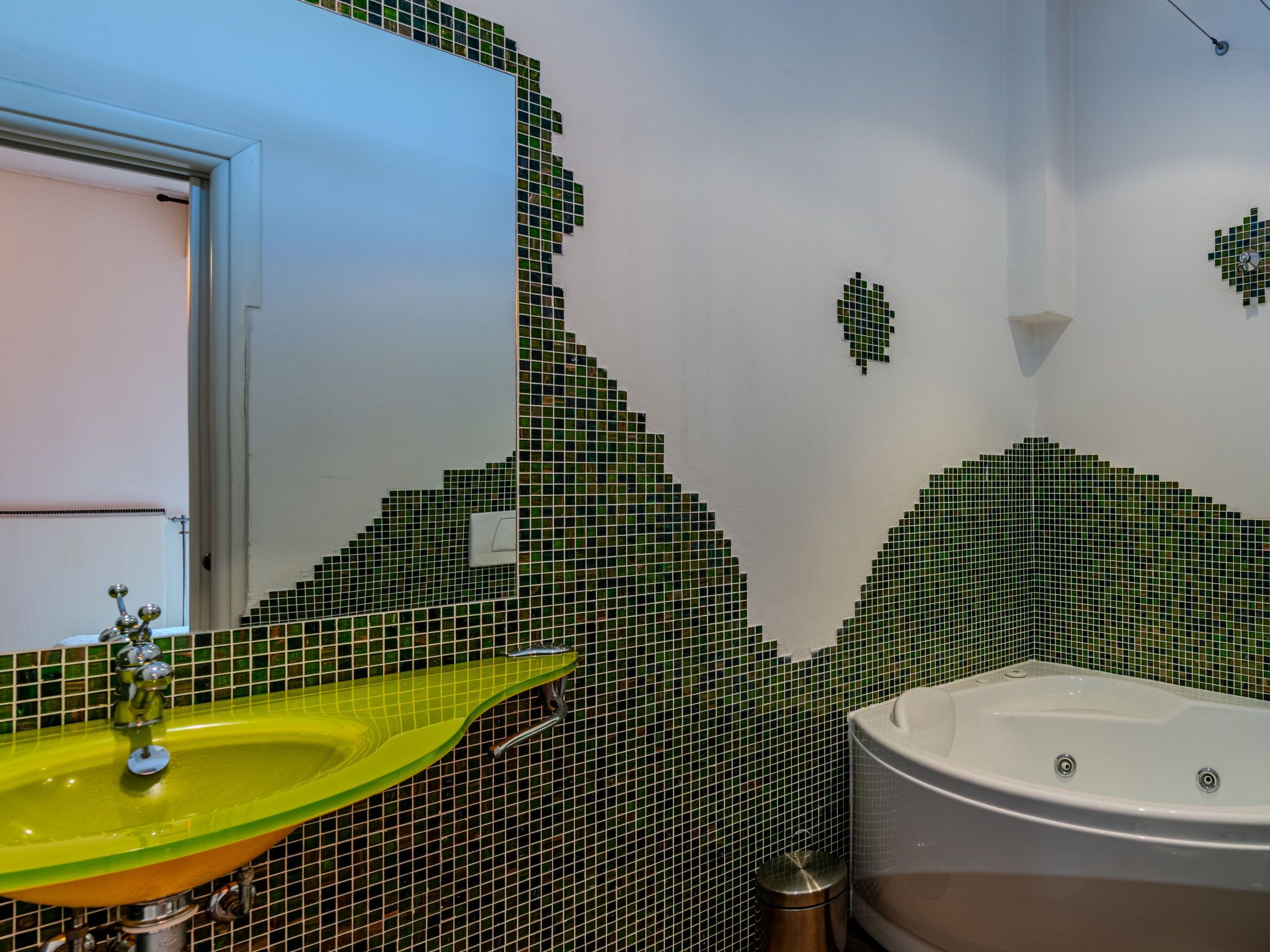 A bathroom with a green mosaic wall, a yellow sink, and a white bathtub.