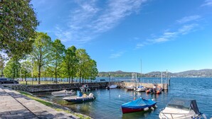 A marina with boats docked, a stone walkway, and a view of the water and hills in the background. - Attilio lake front view by Interhome (Ispra)