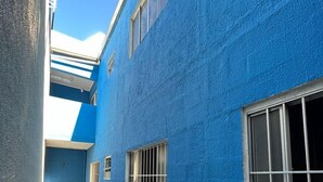 A narrow corridor with a blue exterior wall, a tiled floor, and a window with metal bars. - ALOJAMENTO POUSADA (Campinas)