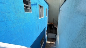 A narrow alleyway with a blue building on one side and a grey building on the other. There are windows and a small door visible on the blue building. - ALOJAMENTO POUSADA (Campinas)