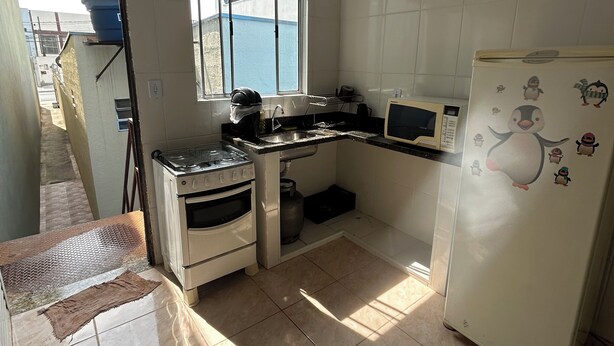 A kitchen with white cabinets, a stove, a sink, and a refrigerator with penguin stickers. - ALOJAMENTO POUSADA (Campinas)