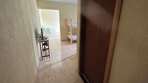 A hallway with a wooden door, a desk with a computer, and a bunk bed in the background. - ALOJAMENTO POUSADA (Campinas)