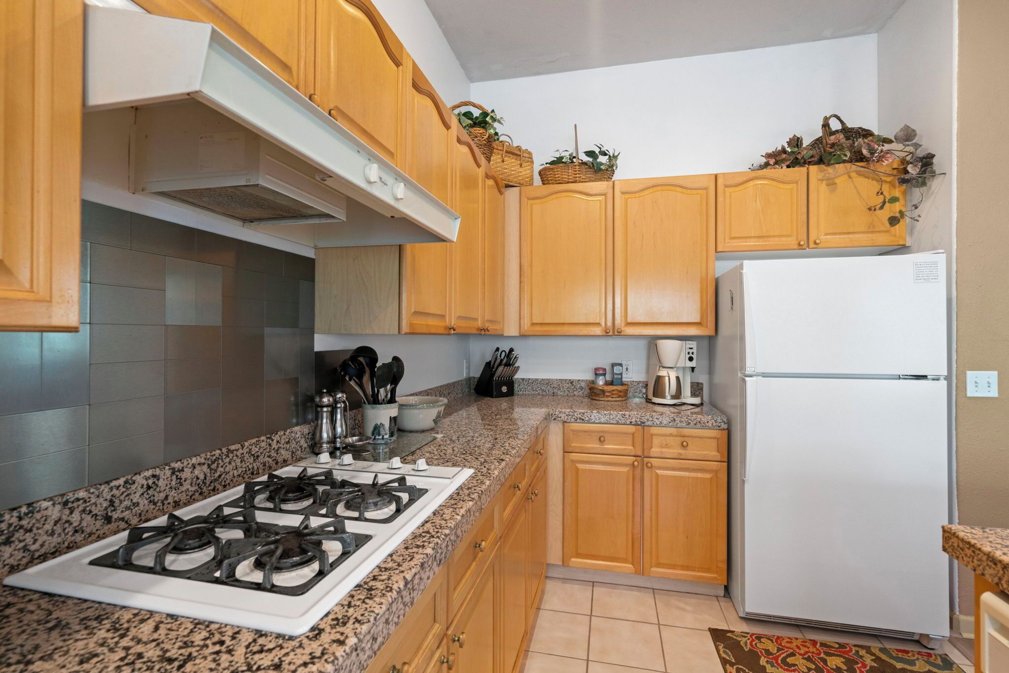 A kitchen with granite countertops, wooden cabinets, a gas stove, a refrigerator, and various kitchen utensils.