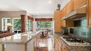 A kitchen with granite countertops, wooden cabinets, a gas stove, and a dining area with a table and chairs.