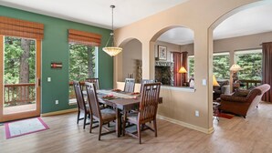A spacious dining area with a wooden table and chairs, a stone fireplace, and large windows with blinds.