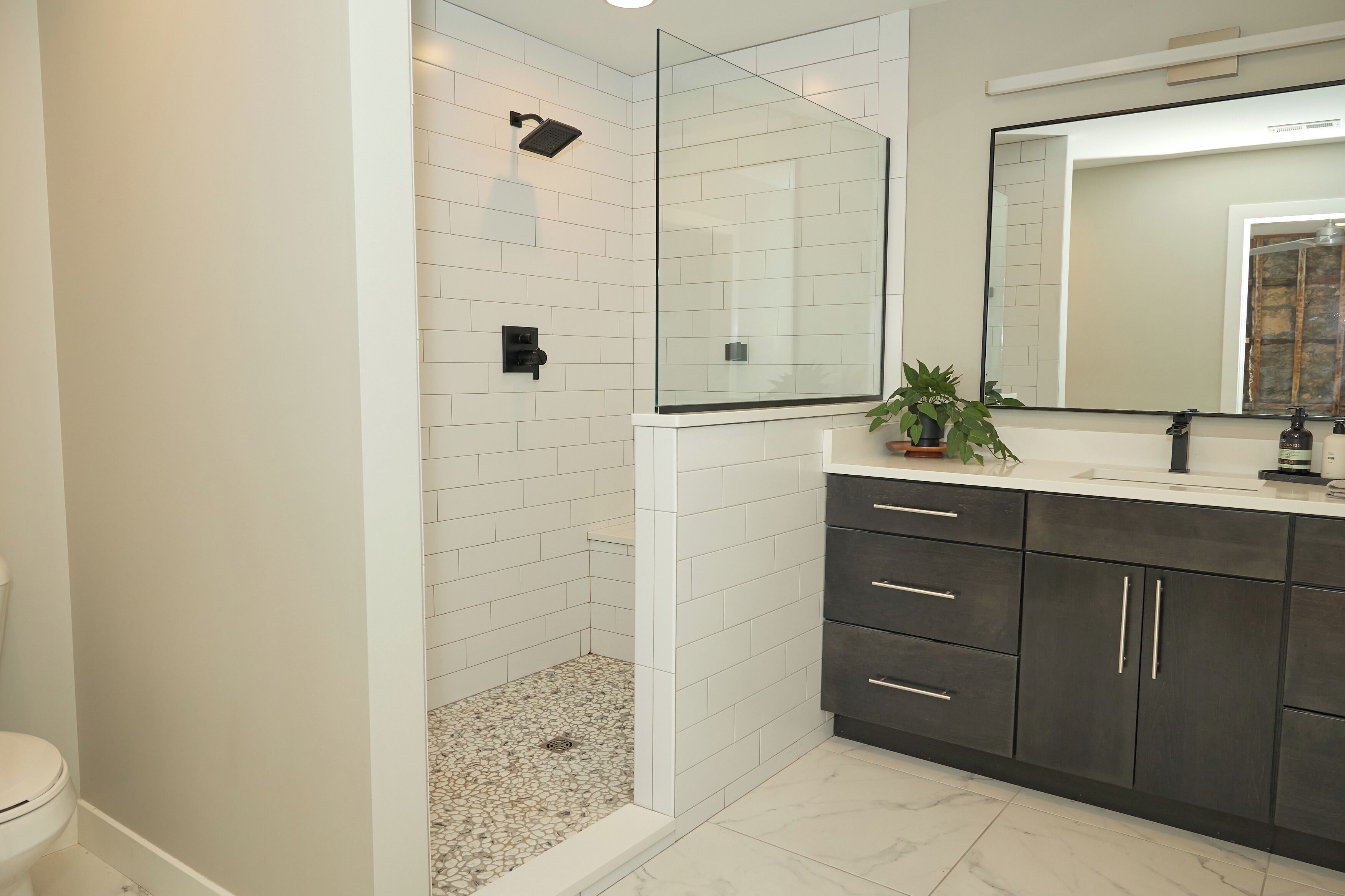 A modern bathroom with a glass-enclosed shower, white tiled walls, a dark wooden vanity, and a large mirror.