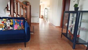 Un salon avec un canapé bleu, une vitrine contenant des services à thé et un escalier menant à une autre pièce.
