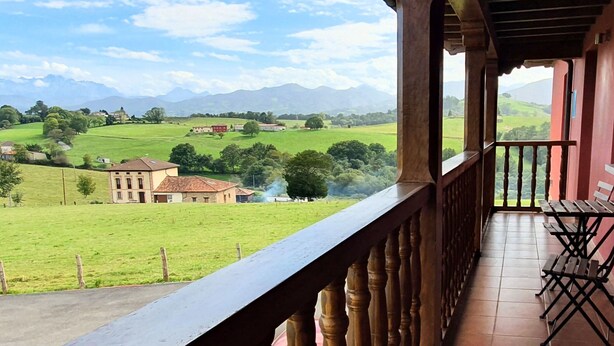 Un balcon donnant sur un champ verdoyant et des montagnes lointaines.