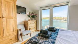 Un dormitorio con una cama grande, un armario de madera, una silla, un tocador, un televisor y vistas al mar.