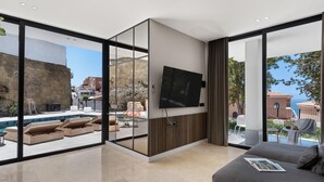 Una sala moderna con televisor grande, sofá y vista a la piscina.