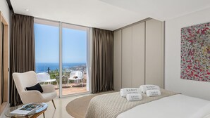 Una habitación de hotel moderna con una cama grande, una zona de estar con una mesita de cristal y un balcón con vistas al mar.