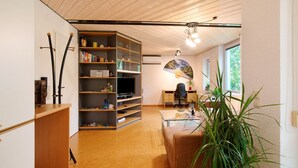 A modern living room with a wooden ceiling, a bookshelf, a television, a glass coffee table, and a large plant. - Apartment 'Stumpp´s Appartement' with Private Terrace, Wi-Fi and Air Conditioning (Heroldstatt)