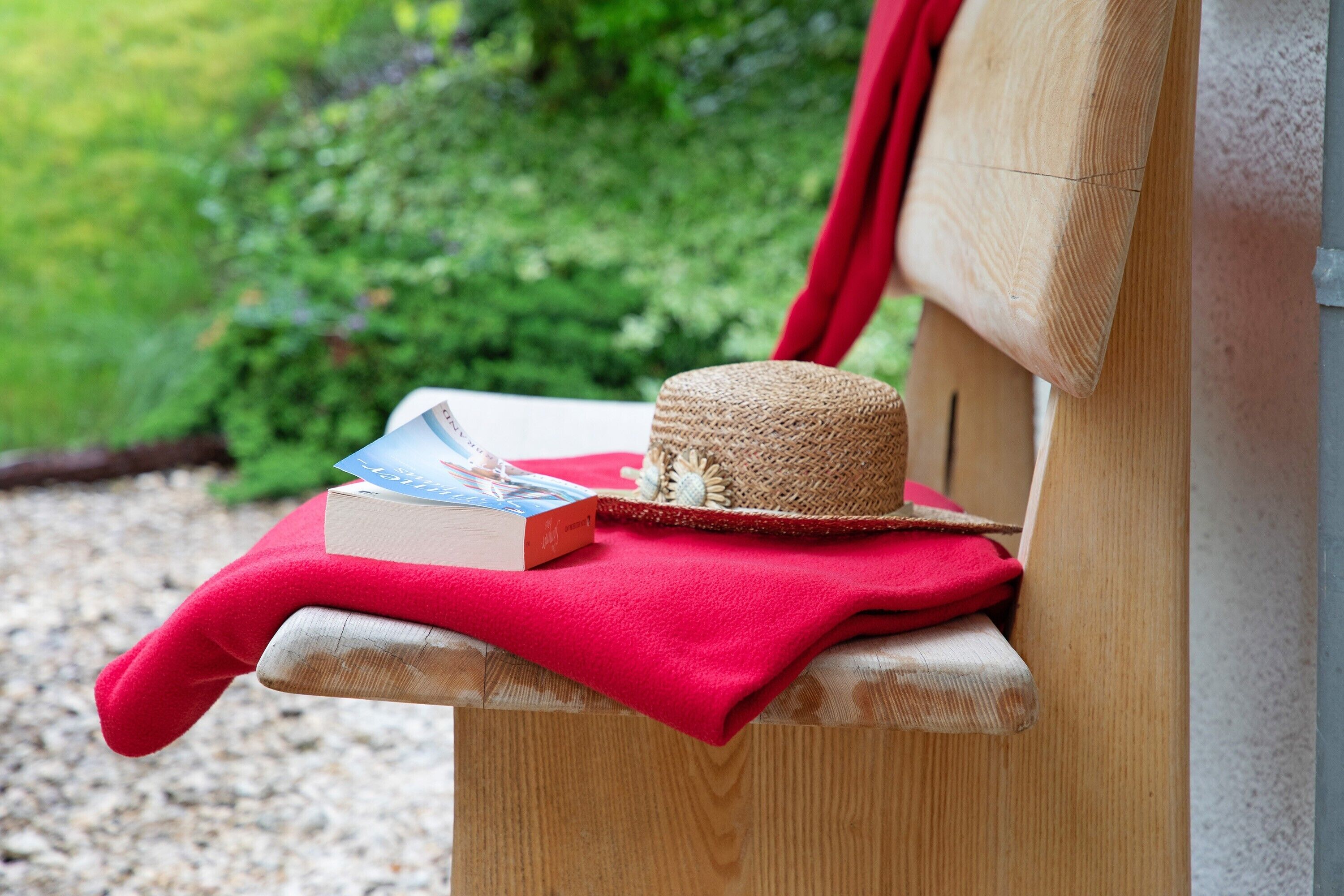 A wooden bench with a red cloth, a straw hat, and a book.