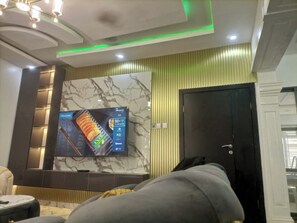 A modern living room with a large flat-screen TV, a marble wall, and a black door.