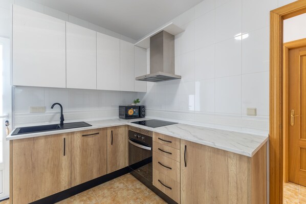Una cocina moderna con armarios blancos, un lavamanos negro y un horno empotrado.