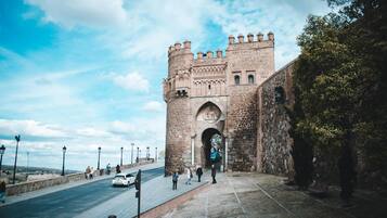 A historic stone gate with a large archway, leading to a paved pathway and a view of the city in the distance.