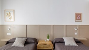 A hotel room with two beds, a small wooden table with a plant, and wall-mounted light switches. - Callejón del Pozo V, accommodation Puy du Fou (Galvez)