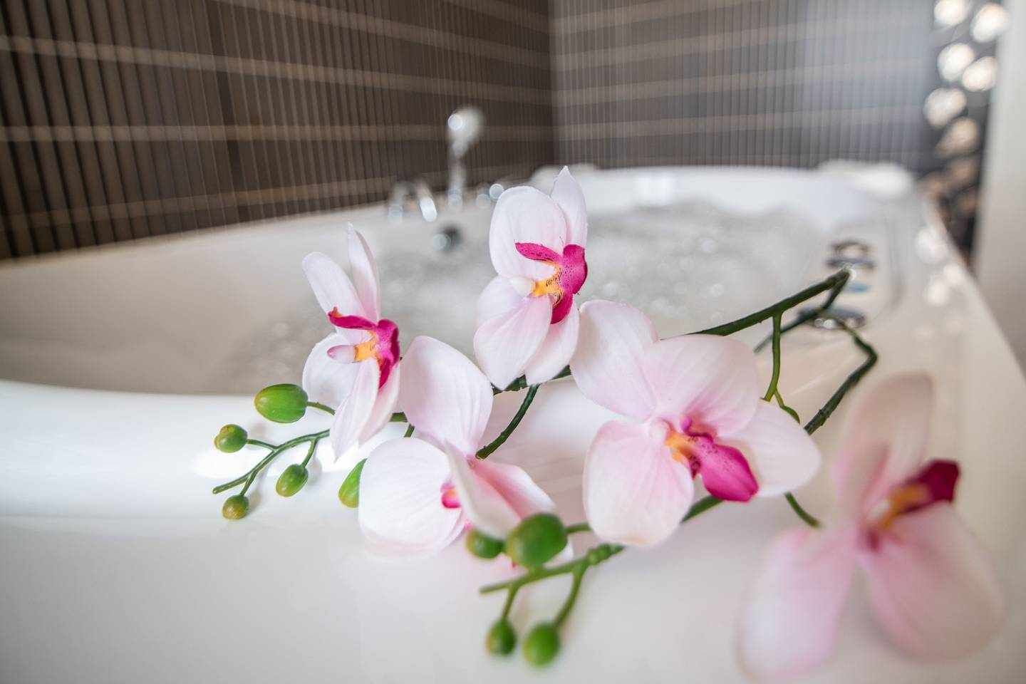 Eine Badewanne mit Wasser, umgeben von rosafarbenen Orchideen.