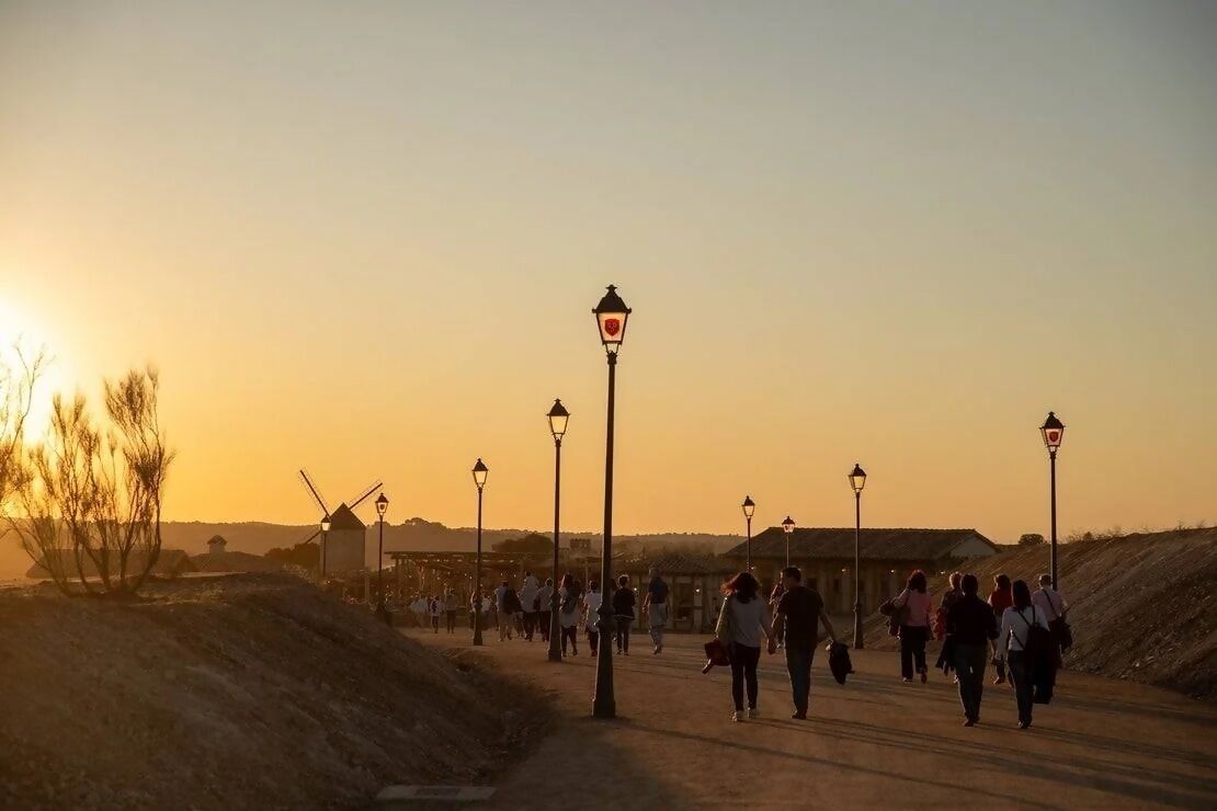 A sunset scene with people walking on a path, street lamps, and windmills in the background.