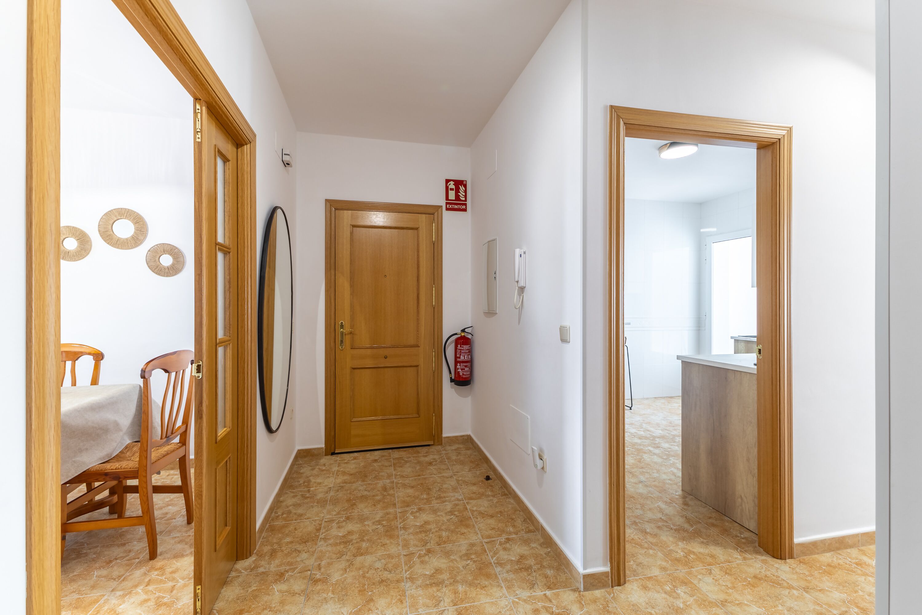 A hallway with a wooden door, a fire extinguisher, and a table with chairs.