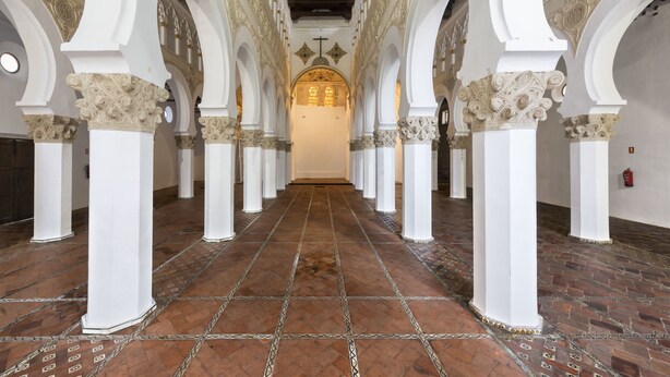 A corridor with white columns and patterned floor tiles leading to a central area with a cross and illuminated windows. - Callejón del Pozo V, accommodation Puy du Fou (Galvez)