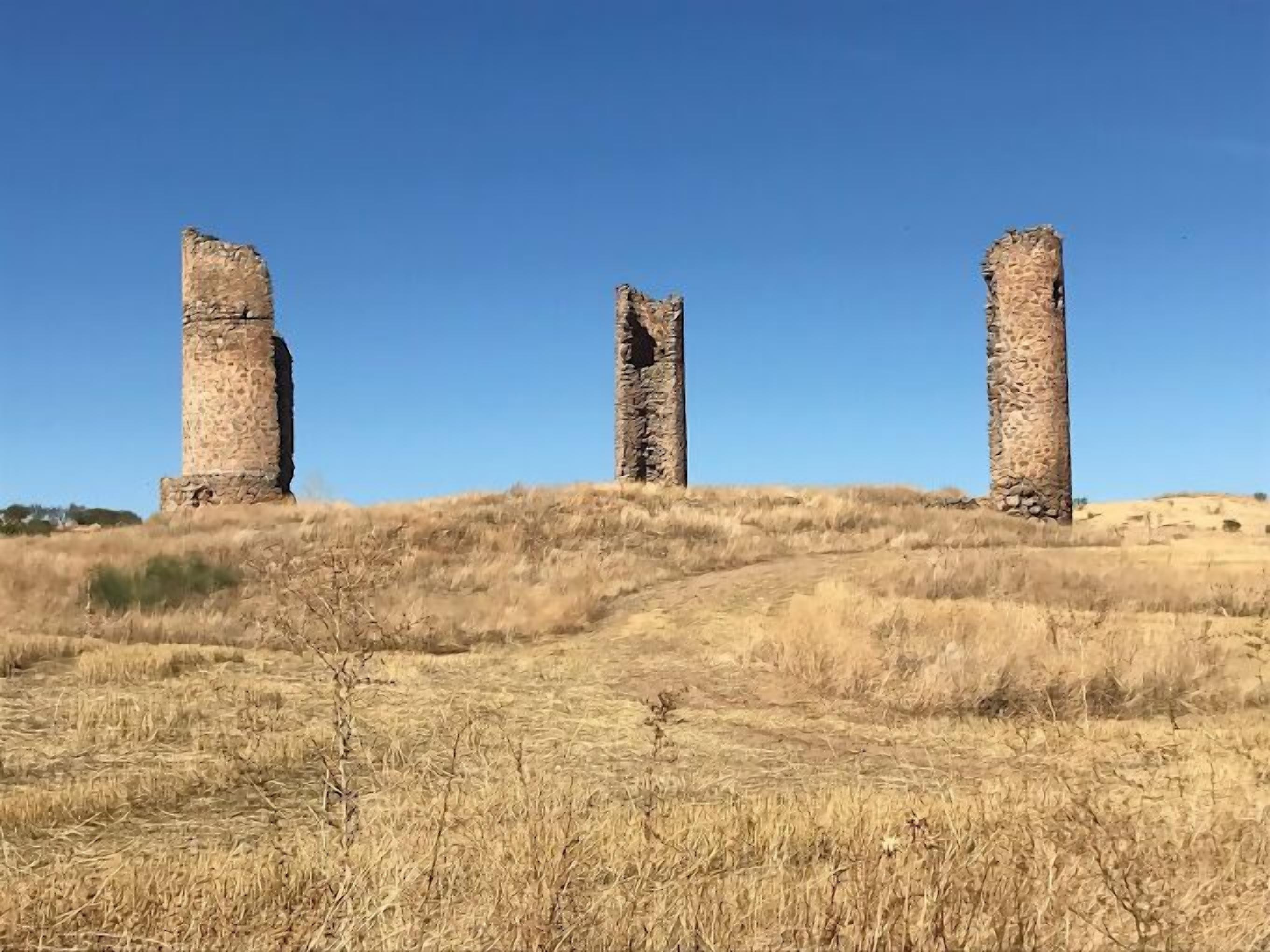 Three stone pillars on a grassy hill under a clear sky.