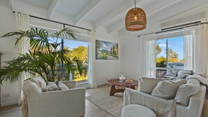 A spacious living room with a large plant, a sofa, a coffee table, and a hanging light fixture. - Lake Metung | Modern Lake House Escape (Metung)