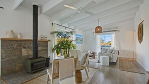 A spacious living room with a stone fireplace, a large window with a view, a ceiling fan, and a cozy seating area. - Lake Metung | Modern Lake House Escape (Metung)