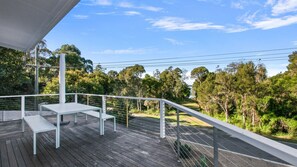 A wooden deck with a table and benches, overlooking a road and dense trees. - Lake Metung | Opposite the Lake, Kayaks & Firepit (Metung)