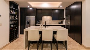 Una cocina moderna con una isla central, muebles oscuros y una estantería para vinos a la izquierda.