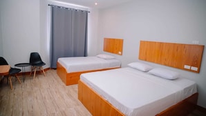 Ein Hotelzimmer mit zwei Einzelbetten, einem kleinen Tisch mit Stühlen und einem großen Fenster mit Vorhängen.