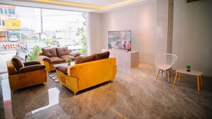 Eine moderne Lobby mit einem gelben Sofa, braunen Sesseln, einem weißen Stuhl und einem kleinen Tisch mit einer Pflanze.