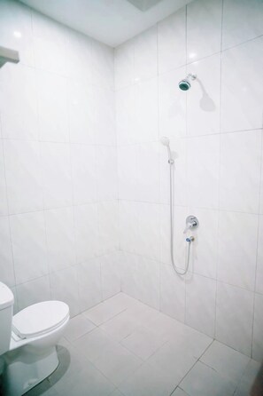 Une salle de bain comprenant des toilettes, une douche avec un pommeau de douche amovible et un robinet mural.
