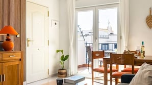 Een gezellige woonkamer met een houten kast, een tafel met boeken en een lamp, een kamerplant en uitzicht op het buitenbalkon.