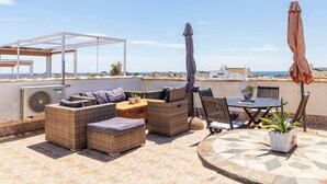 Een terras op het dak met rieten meubels, een tafel en stoelen, met uitzicht op de kust.