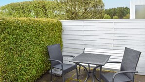 Een terras buiten, met een witte hek, twee stoelen en een tafel.