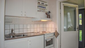 Een compacte keuken met witte kastjes, een gasfornuis, een spoelbak en een raam met geëtste glas.