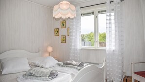 Een opgemaakt bed met kussens en dekens, een bedlampje en een raam met dunne gordijnen.